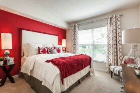 Bedroom with carpeted floor, large window, and tall bed with pillows and linens.
