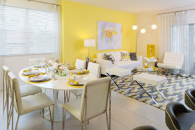 Dining and living room with large rug, modern couch and chairs, and six person dining table with place settings.