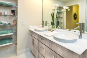 Bathroom with smooth tile floors, dual vanity, and shelves with a selection of towels and soaps.