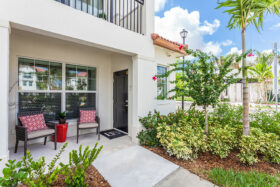 Apartment door patio space with two chairs, overhead balcony, and lush landscaped pathway.
